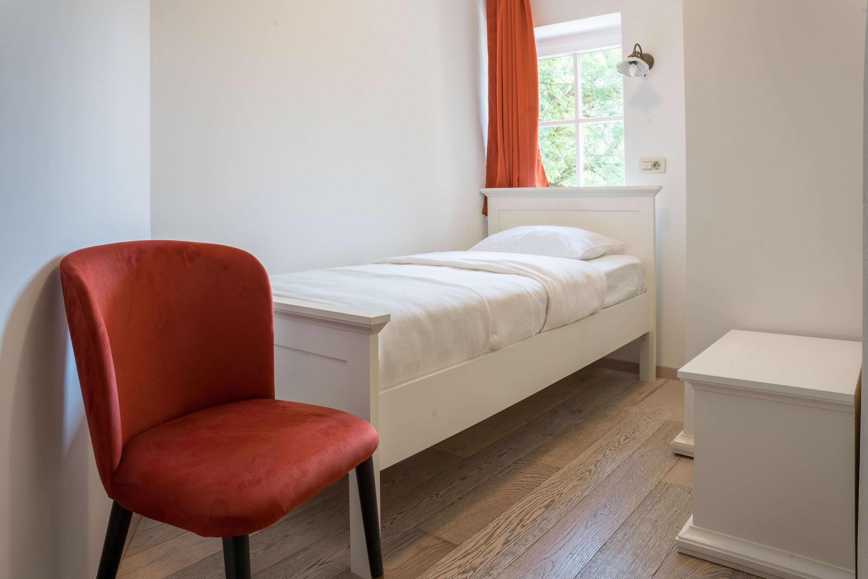 A small, neatly arranged bedroom with a single bed, a chair, and a nightstand.