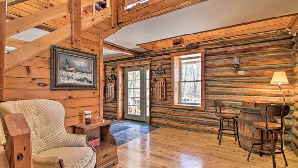 A log cabin interior with a checkered armchair, wooden dining table, and a painting of a snowy landscape. - Spacious Mtn Cabin on 7 Private Acres in Athol! (Athol)