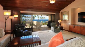 A spacious living area with a balcony, leather sofas, a glass coffee table, and a television. - Cozy Treasure Nestled on a Lush Oceanfront Property - Wailea Elua 1508 (Wailea, Maui)