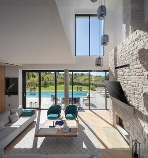 Uma sala de estar moderna com uma janela grande, lareira de pedra e vista para a piscina.