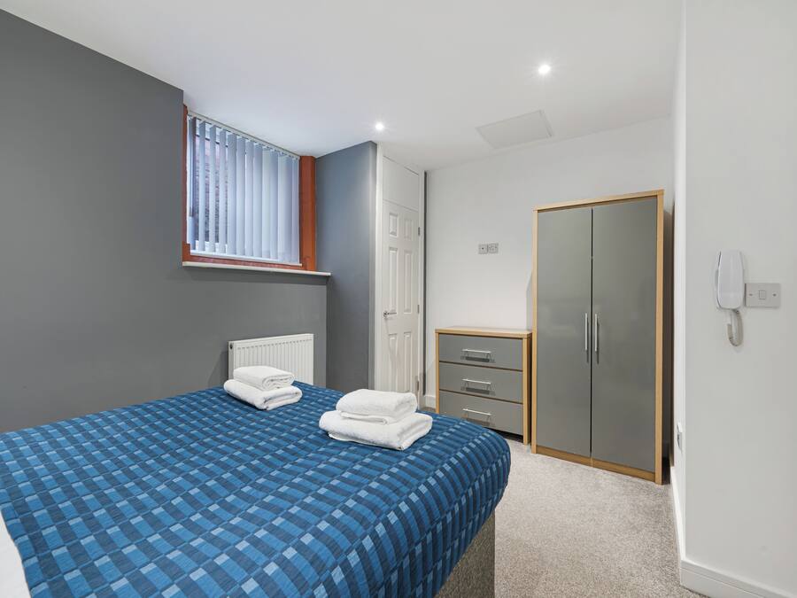 A bedroom with a bed, a wardrobe, a radiator, and a window with blinds.