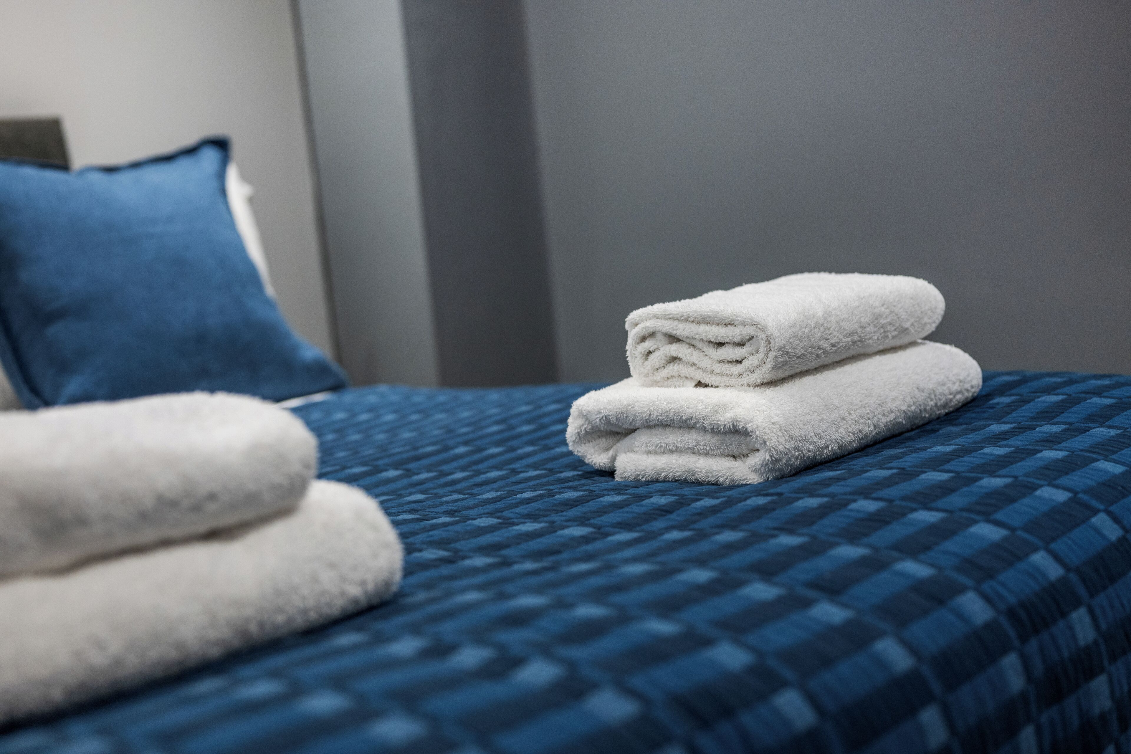 A neatly made bed with a blue checkered bedspread and two folded white towels.
