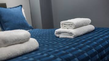 A neatly made bed with a blue checkered bedspread and two folded white towels.