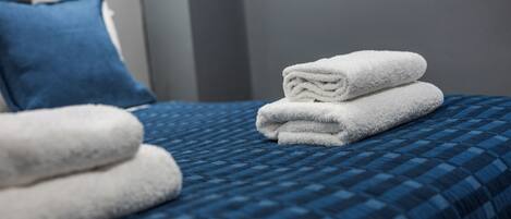 A neatly made bed with a blue checkered bedspread and two folded white towels.