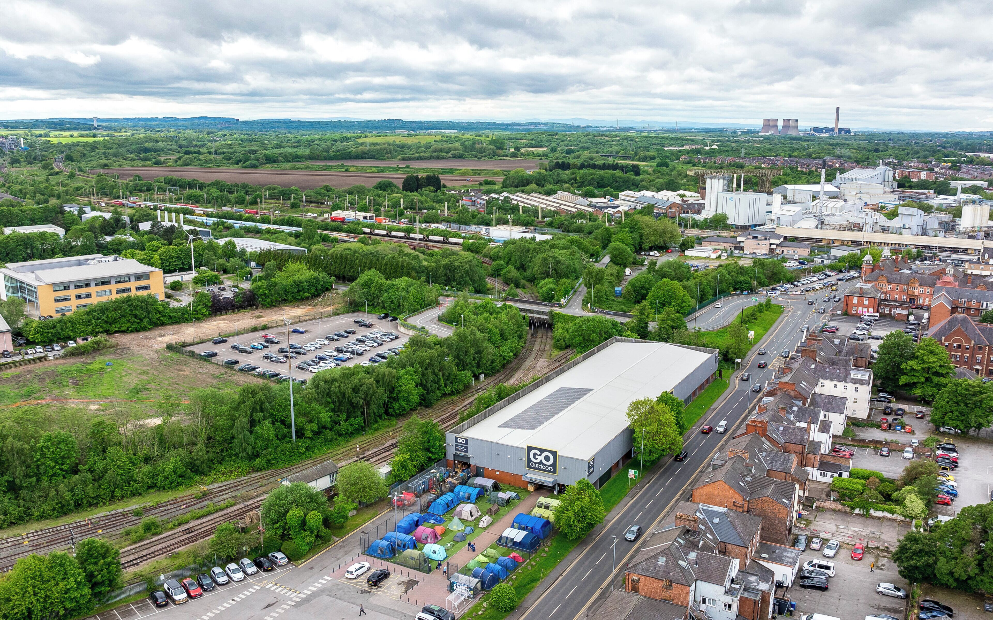 An industrial area with a large warehouse, railway tracks, and a parking lot.