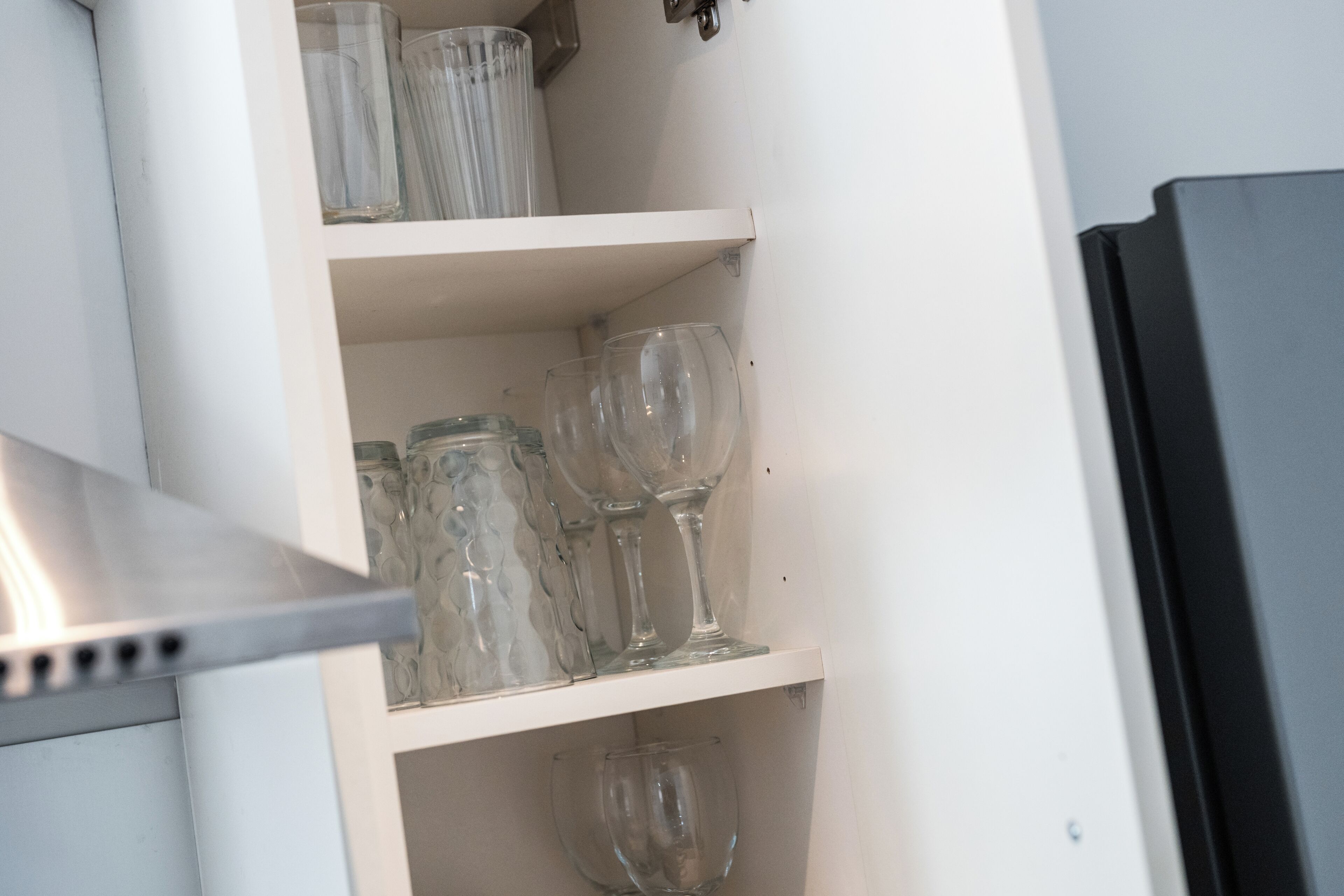 A kitchen with a white cabinet containing glassware and a stainless steel range hood.