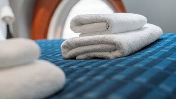 A neatly folded white towel on a blue textured bedspread, with a window in the background.