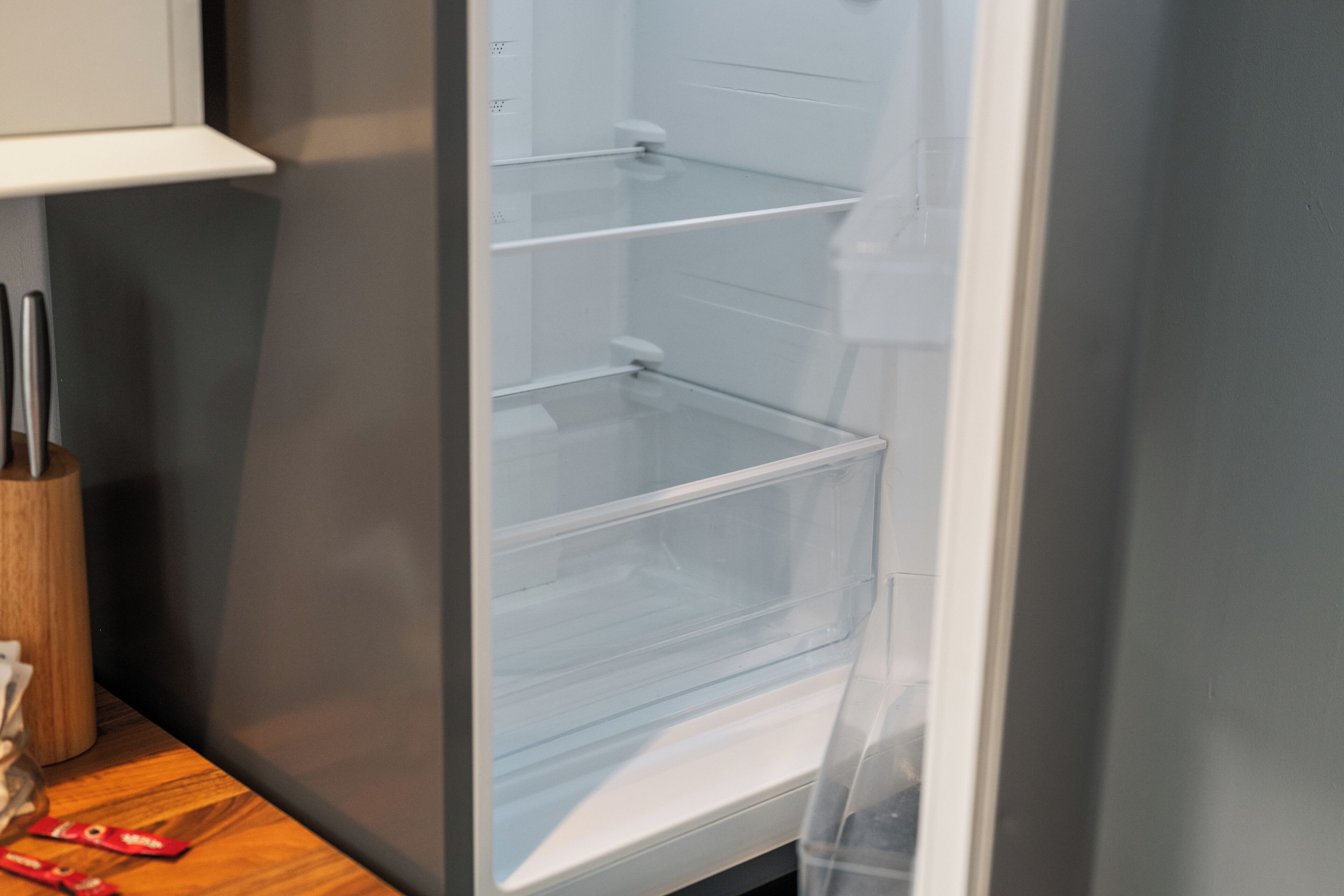 Vue intérieure d’une cuisine moderne dotée d’un réfrigérateur encastré, d’un plan de travail en bois et d’une porte en verre transparent.