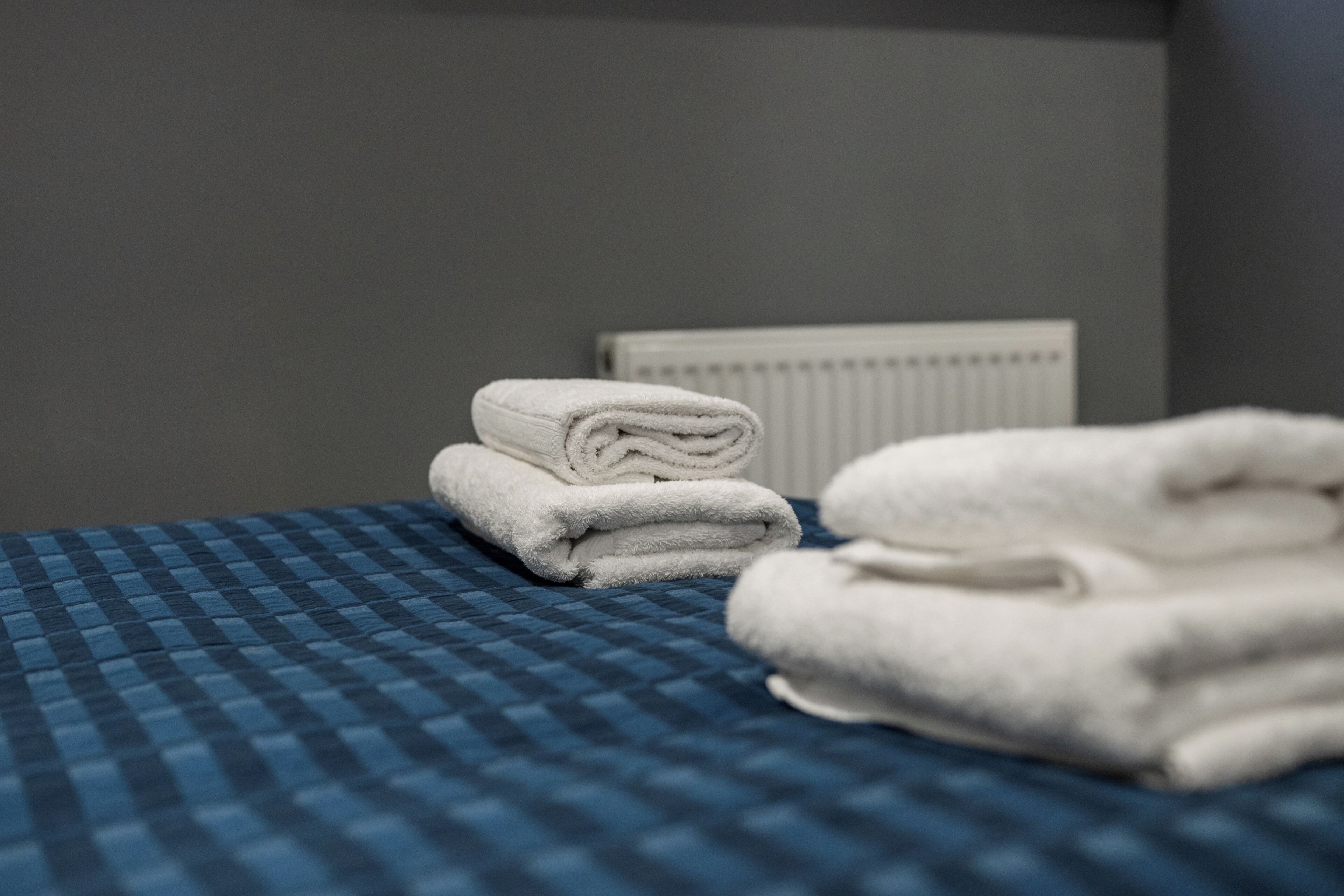 Un lit bien fait, recouvert d’une couverture à carreaux bleus et agrémenté de deux serviettes blanches pliées.