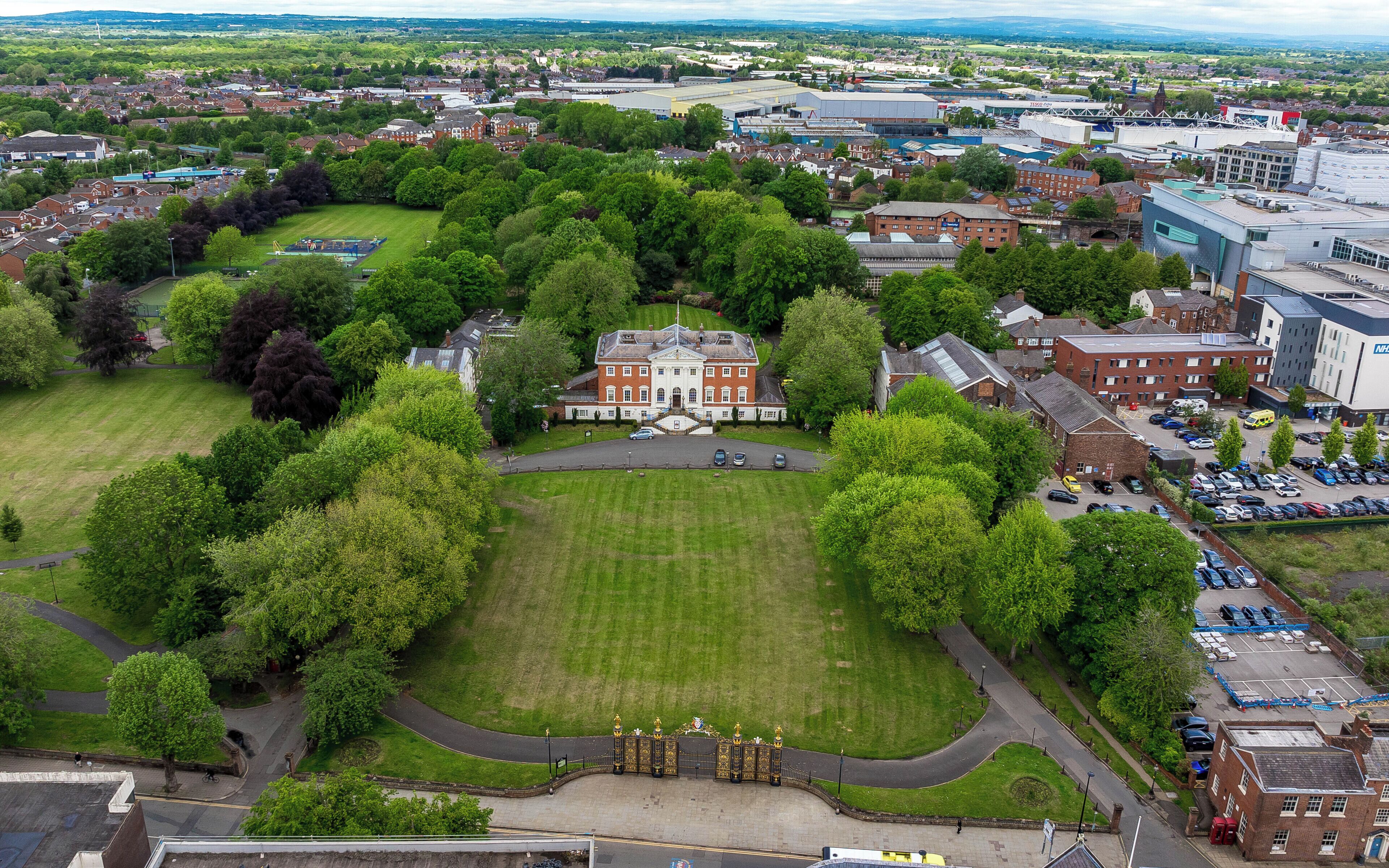 An aerial view of a large estate with a central building, surrounded by lush greenery and a well-maintained lawn.