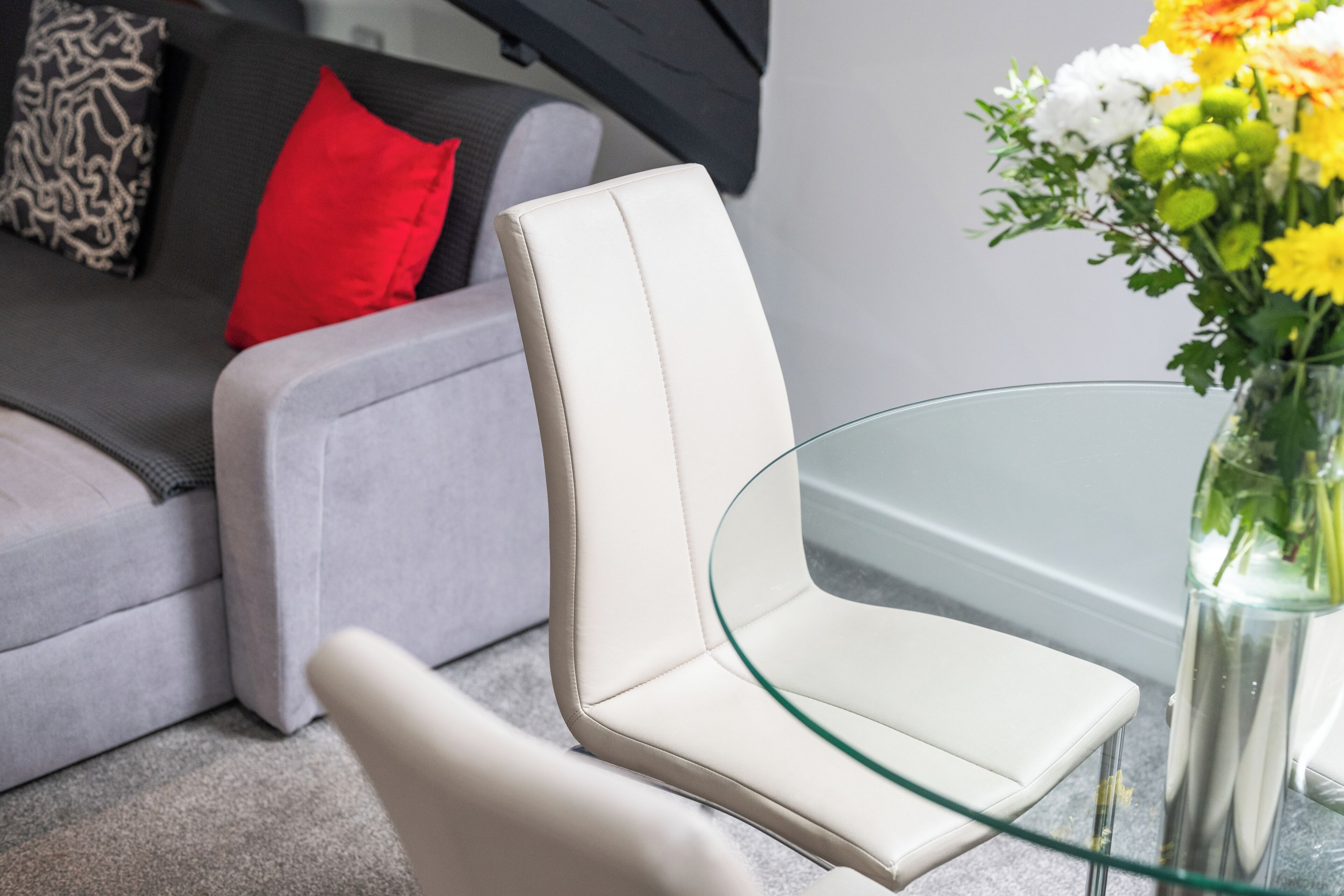 A modern living room with a white leather sofa, a glass coffee table, and a vase with flowers.
