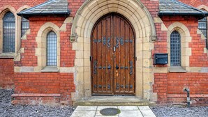 A red brick building with a large wooden double door, arched windows, and a small mailbox. - Emmanuel Church Apartments (Warrington)