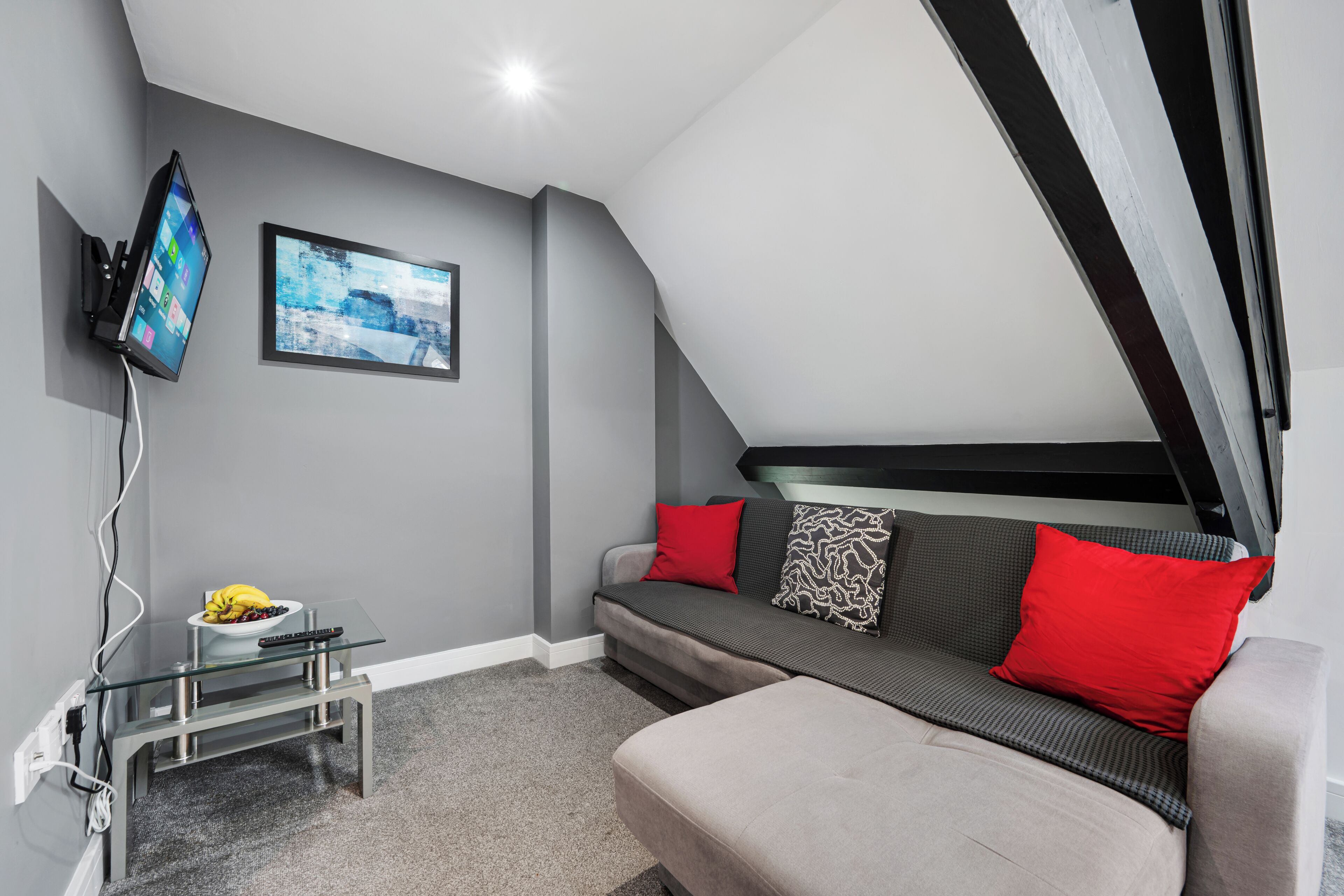 A modern living room with a sofa, a flat-screen TV mounted on the wall, and a glass coffee table.