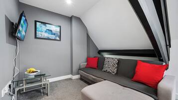 A modern living room with a sofa, a flat-screen TV mounted on the wall, and a glass coffee table.