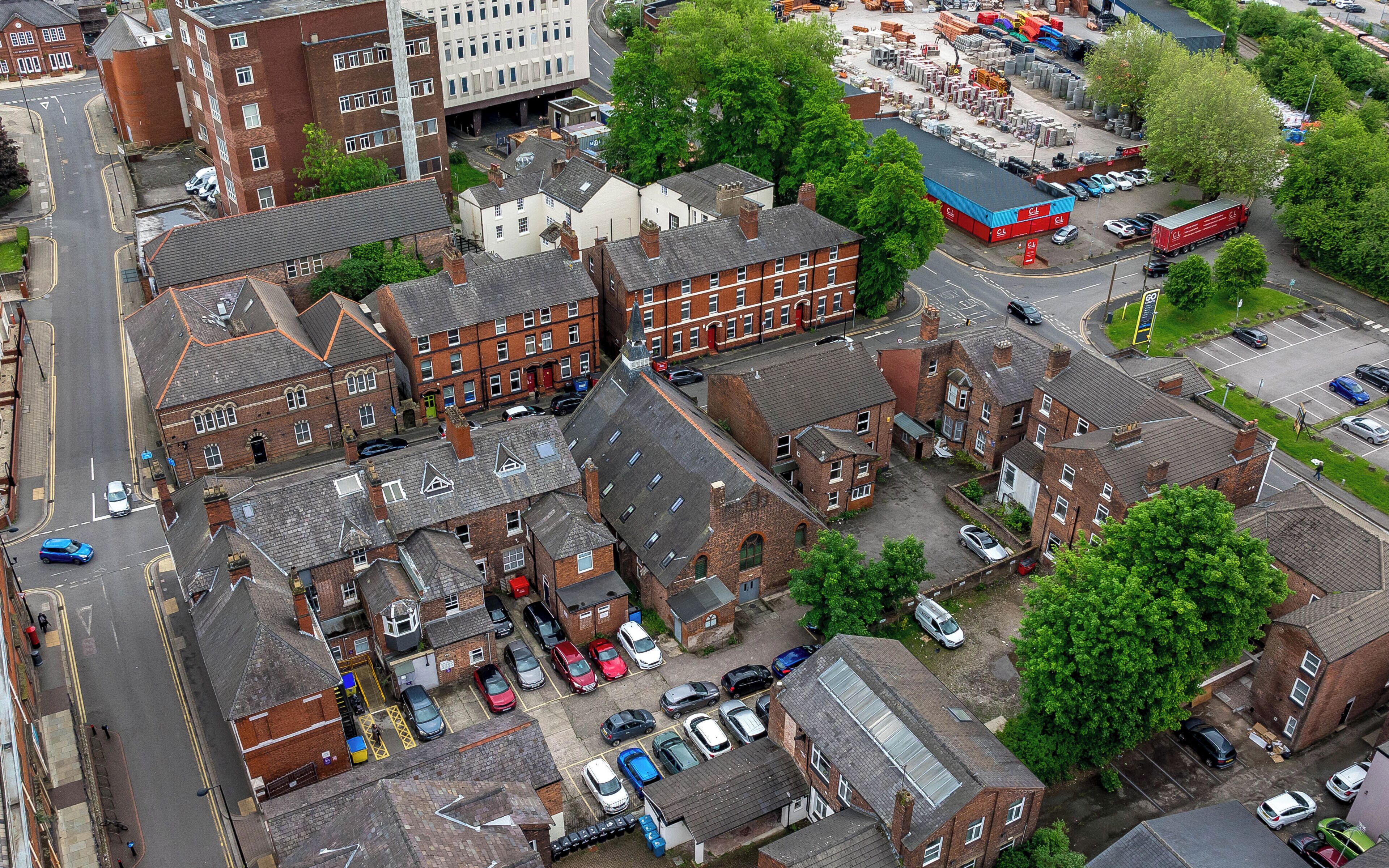 An aerial view of a residential area with multiple brick buildings, a parking lot, and a large industrial facility in the background.