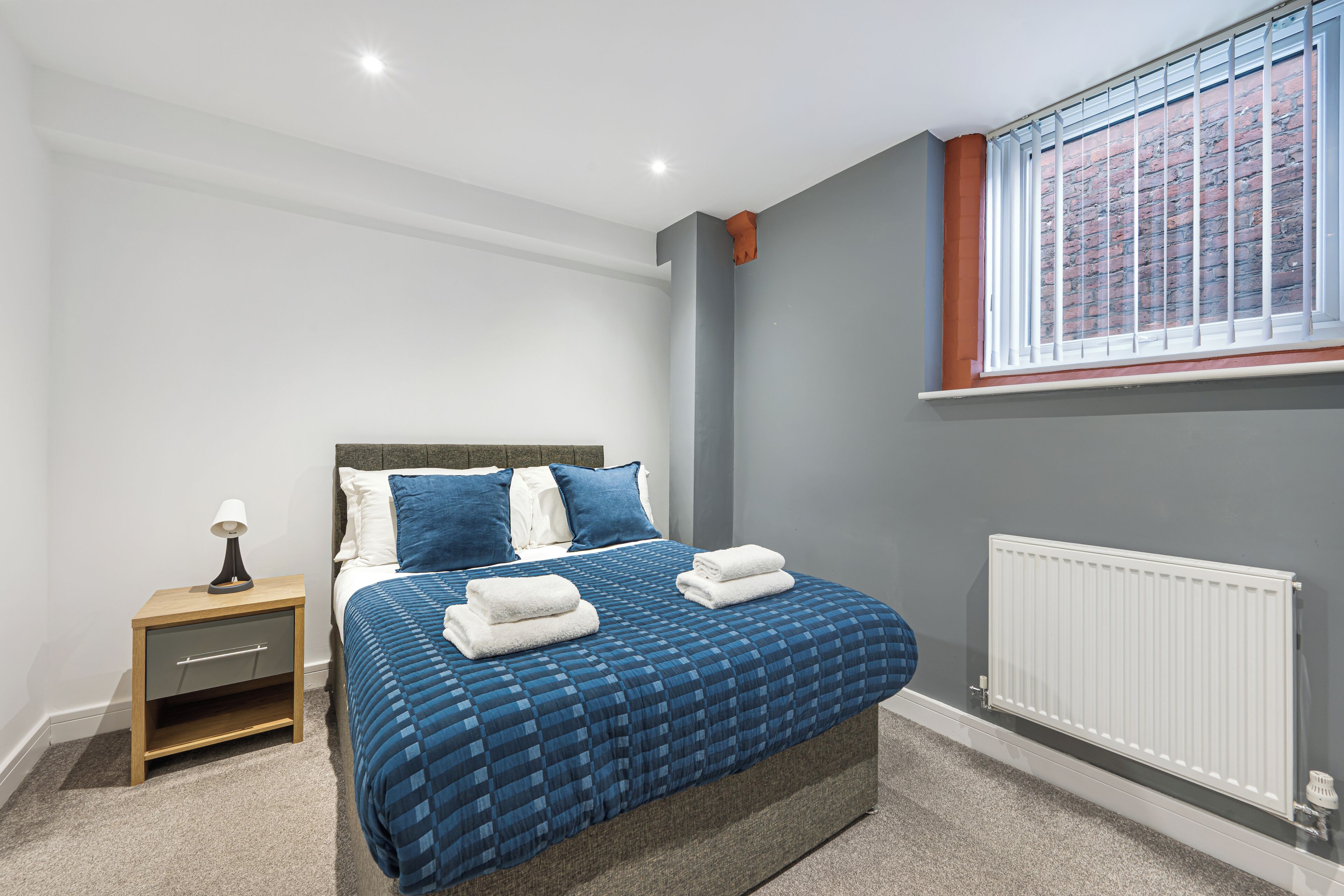 A bedroom with a bed, a nightstand, a window, and a radiator.