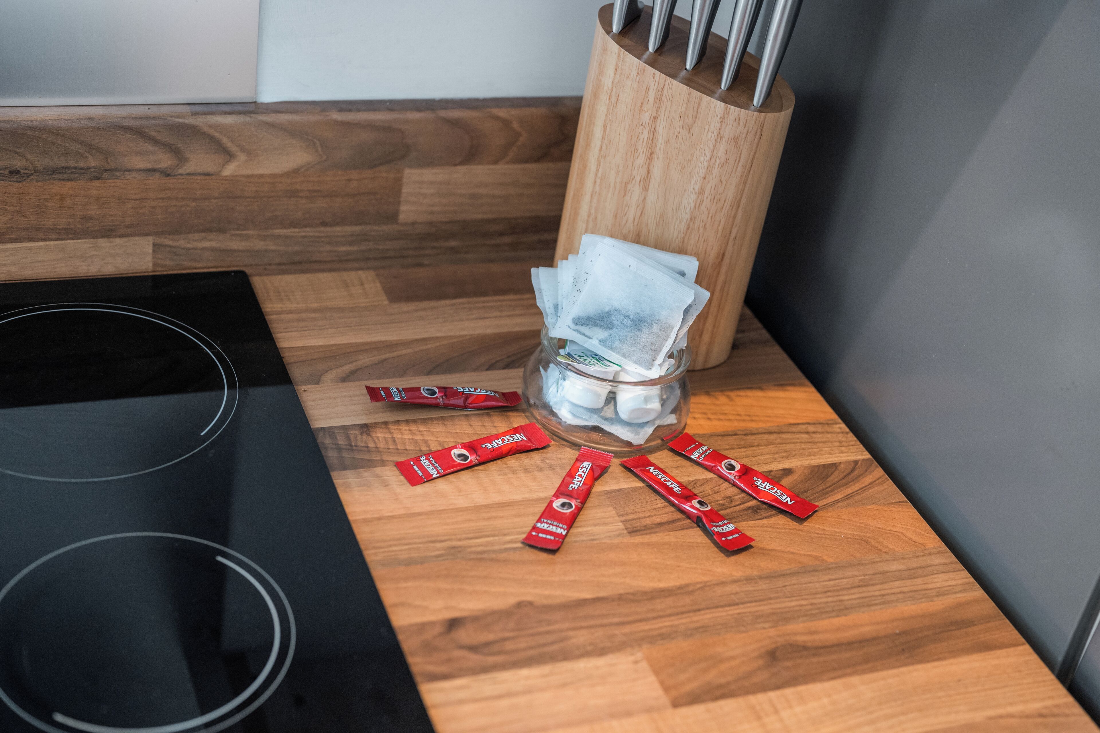 A kitchen with a wooden countertop, a glass jar with utensils, and several red packets.