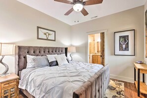 A bedroom with a tufted headboard, a large bed with a quilted duvet, a wooden nightstand, a floor lamp, and a ceiling fan. - Putt-Putt, Pickleball + Trails: Glenville Getaway (Glenville)