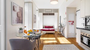 Un espacio habitable compacto con comedor, kitchenette y cama con almohada roja.