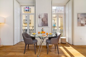 A dining area with a glass table, four grey chairs, and a small round table with fruit and drinks. - Alcântara Premium Studio (Lisbon)