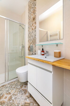 Une salle de bain avec une douche à parois de verre, des toilettes, un lavabo avec un miroir au-dessus et des carreaux de sol à motifs.