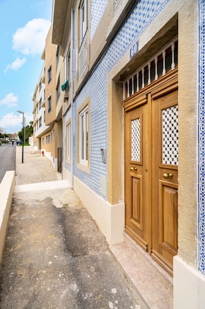 Une vue de rue avec une rangée de bâtiments aux façades ornées de motifs bleus et blancs, une porte en bois avec un panneau de verre décoratif et un ciel dégagé.