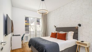 Un dormitorio moderno con una cama grande, televisión, escritorio y vistas al balcón.