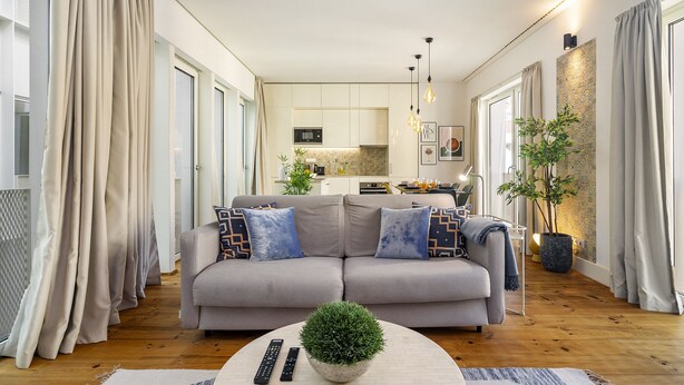 Una sala de estar moderna con un sofá gris, una mesa de centro con una planta y una cocina al fondo.