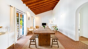 A spacious dining area with a wooden table and benches, white walls, and a tiled floor. - Comporta Family Beach House (Alcacer do Sal)