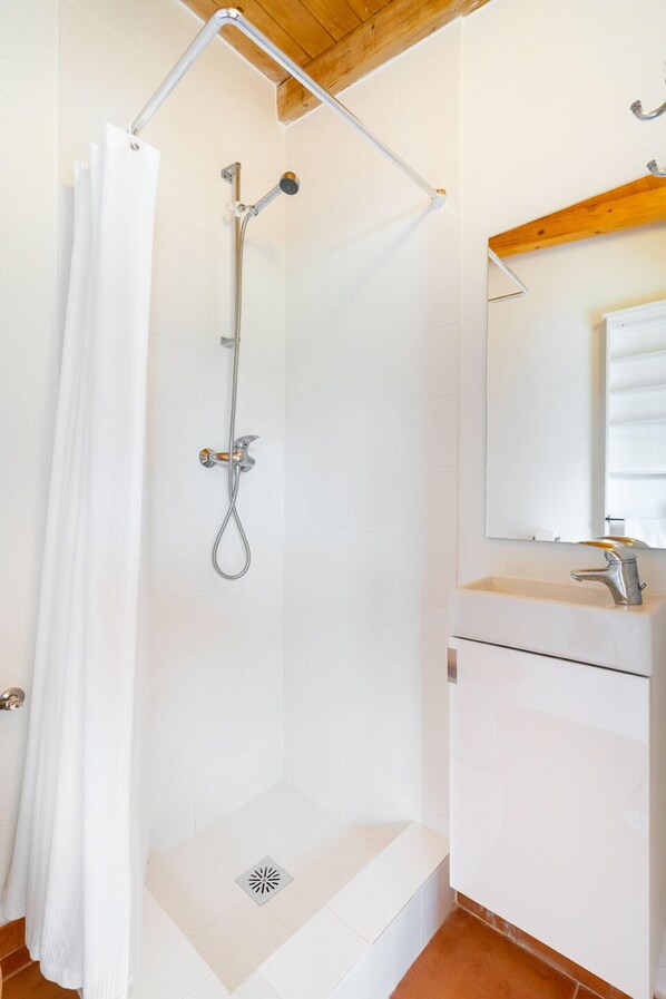 Ducha con barra de apoyo metálica, lavamanos blanco con espejo y techo de madera.