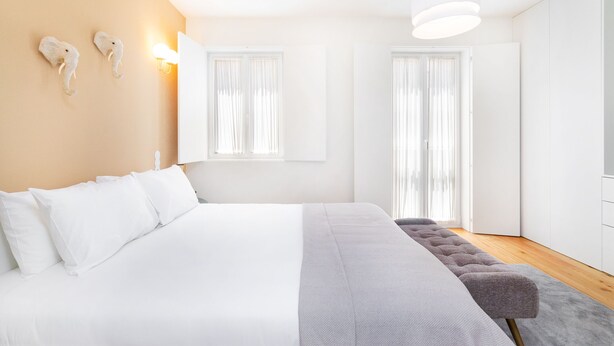 A modern bedroom with a large bed, a bench, and two wall-mounted light fixtures. - CSA18 Premium Design Apartment (Lisbon)