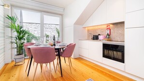 A modern kitchen with white cabinets, a built-in oven, and a dining area with a wooden table and pink chairs. - CSA18 Premium Design Apartment (Lisbon)