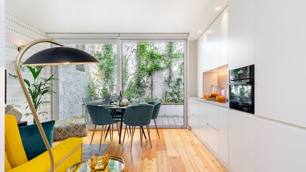 Une cuisine moderne avec des meubles blancs, un coin repas doté d’une table en verre et un fauteuil jaune.