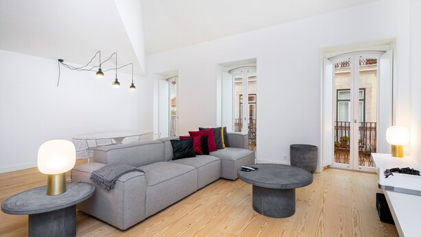 A modern living room with a grey sectional sofa, two round tables, and a ceiling light fixture.