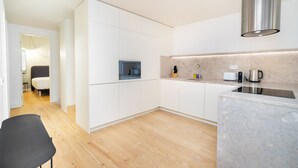 A modern kitchen with white cabinets, a wooden floor, a built-in stove, and a stainless steel range hood.