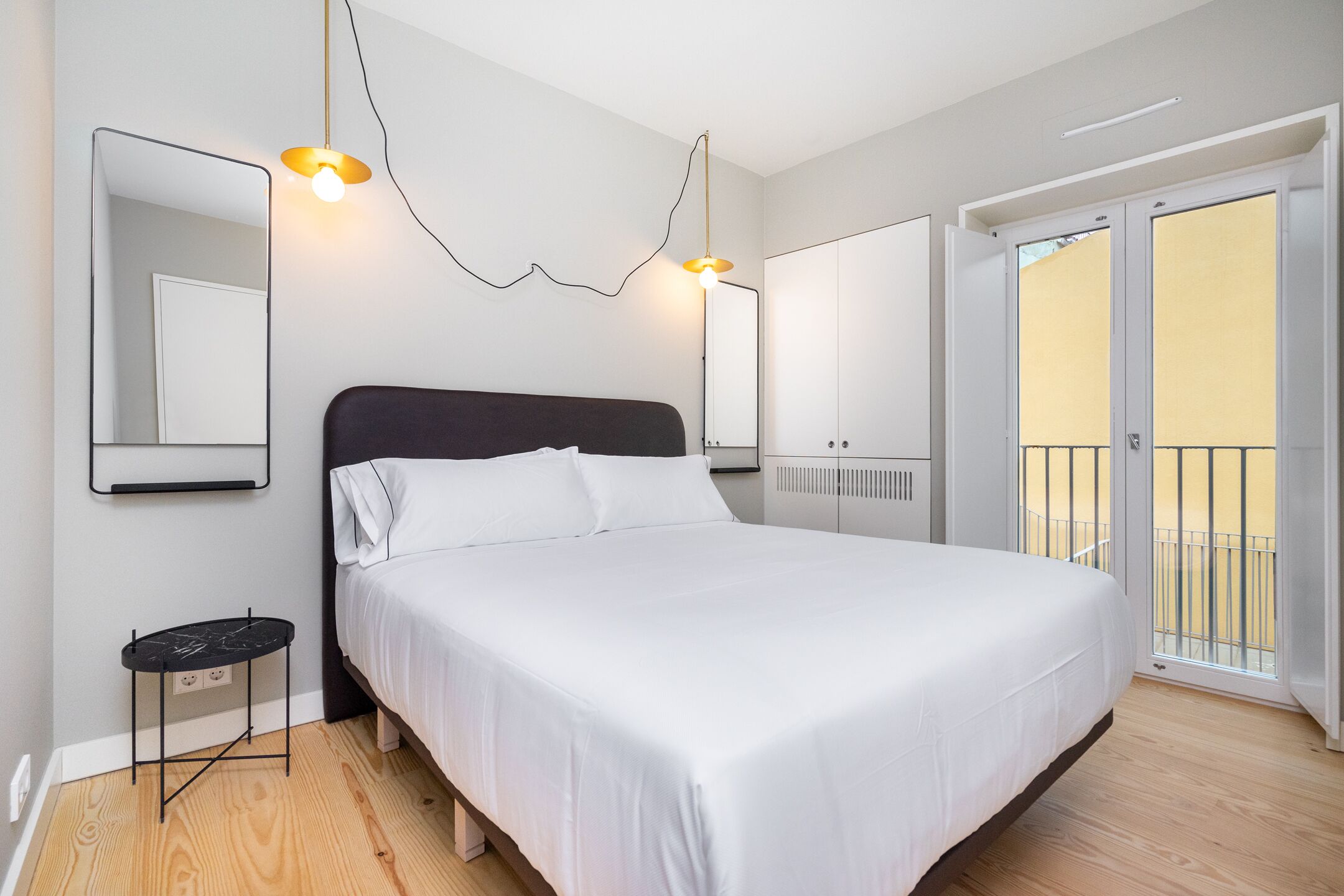 A bedroom with a large bed, a bedside table, a mirror, and a balcony with a railing.