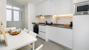 A modern kitchen with white cabinets, a built-in oven, and a countertop with a toaster and kettle. - Hideaway Family Apartment (Lisbon)