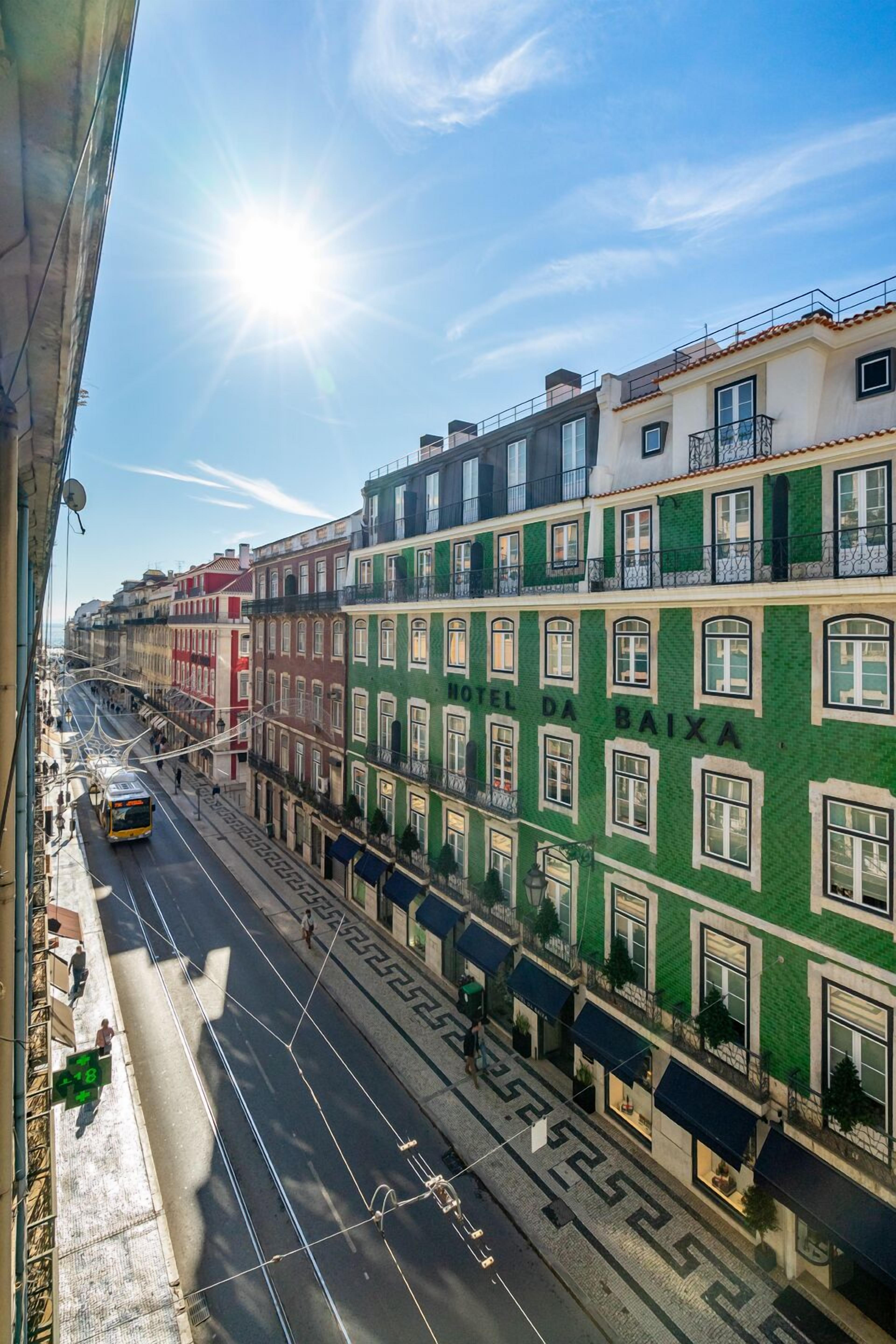 A street view with a building labeled "HOTEL DA BAIXA" featuring a green facade, multiple windows, and balconies.