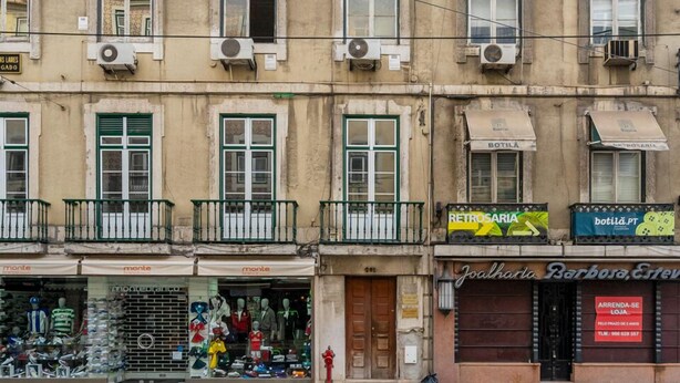 Ein mehrstöckiges Gebäude mit mehreren Geschäften im Erdgeschoss, darunter ein Bekleidungsgeschäft und ein Möbelhaus.