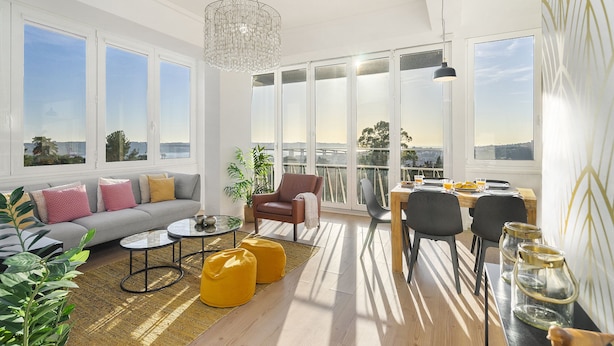 Ein großzügiger Wohnbereich mit Sofa, Couchtisch und Sesseln, großen Fenstern mit Blick und einem Balkon mit Geländer.