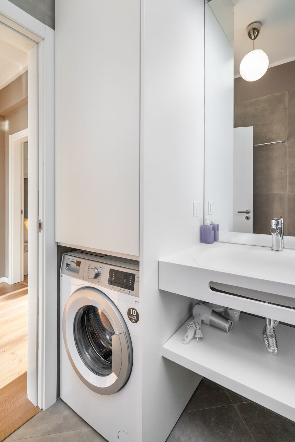 A modern bathroom with a built-in washer and dryer, a large mirror, and a white vanity with a sink.