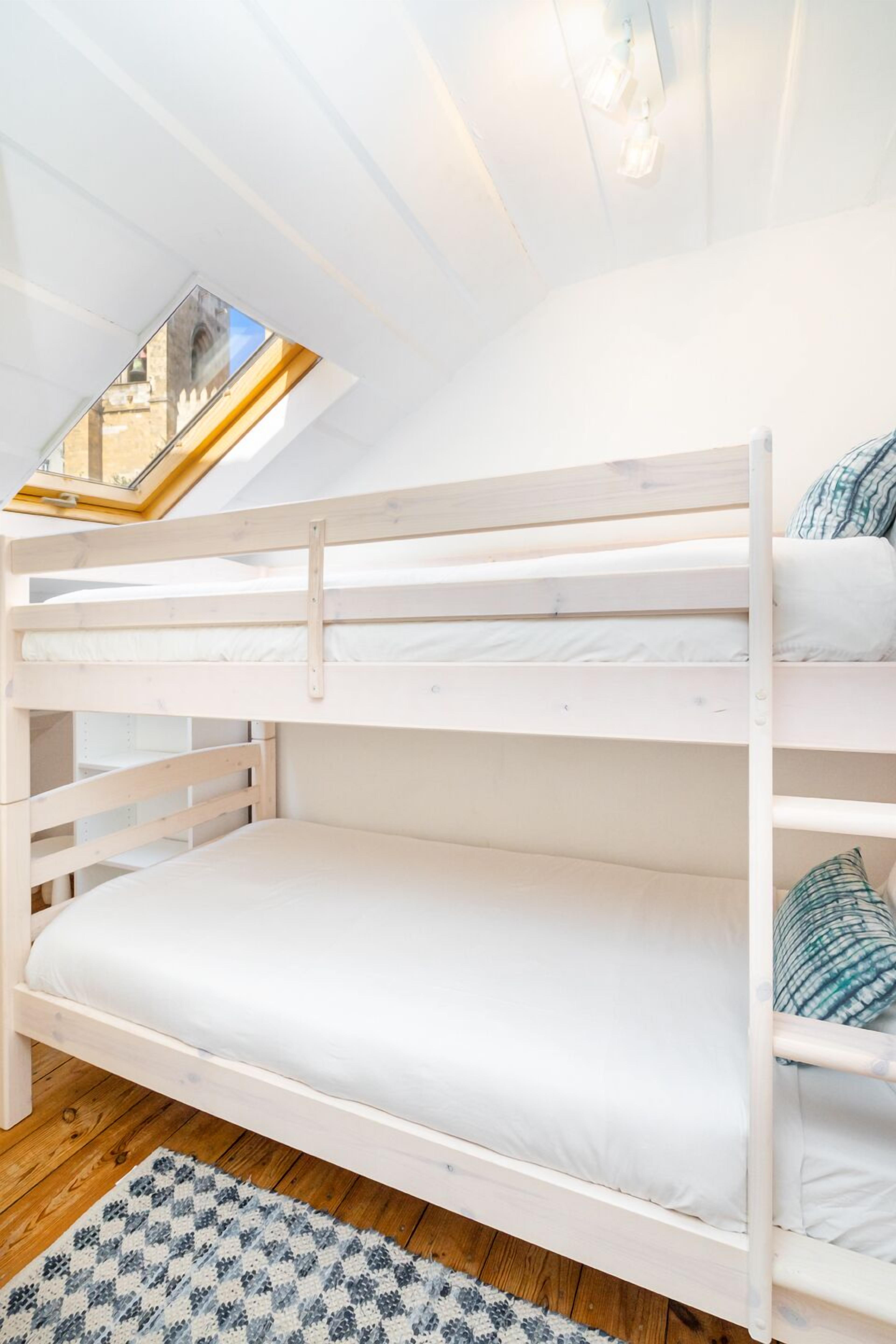 A bunk bed with a skylight, white walls, and a patterned rug.