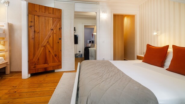 A bedroom with a large bed, wooden door, and a view into another room. - Sé Skyline Apartment (Lisbon)