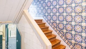 A staircase with a white handrail and wooden steps leading to a room with a patterned tile wall. - Sé Skyline Apartment (Lisbon)