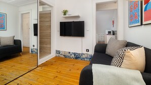A modern living room with a black sofa, a wooden floor, a mounted TV, and a tiled backsplash. - Sé Skyline Apartment (Lisbon)