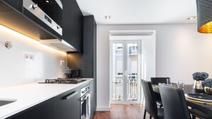 Une cuisine moderne avec un plan de travail noir, des appareils en acier inoxydable et un coin repas comprenant une table et des chaises noires.