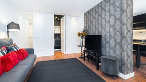 Un salon moderne avec un canapé gris, un tapis noir, un téléviseur et un pouf gris.