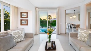 Una sala de estar moderna con un juego de sofá, una mesa de centro con un florero, y vista a una piscina y zona de comedor al aire libre a través de grandes puertas corredizas de vidrio.