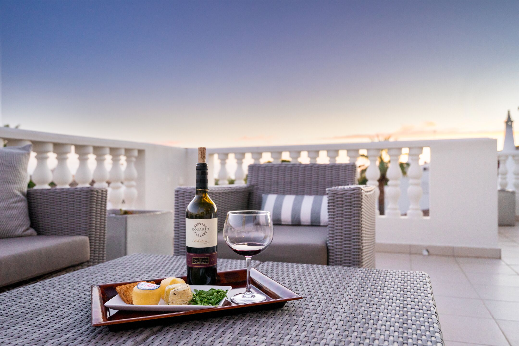 A terrace with wicker furniture, a bottle of wine, and a glass on a tray.
