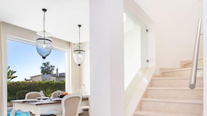 Un interior moderno con una escalera, un comedor con vistas a la piscina e iluminación colgante.